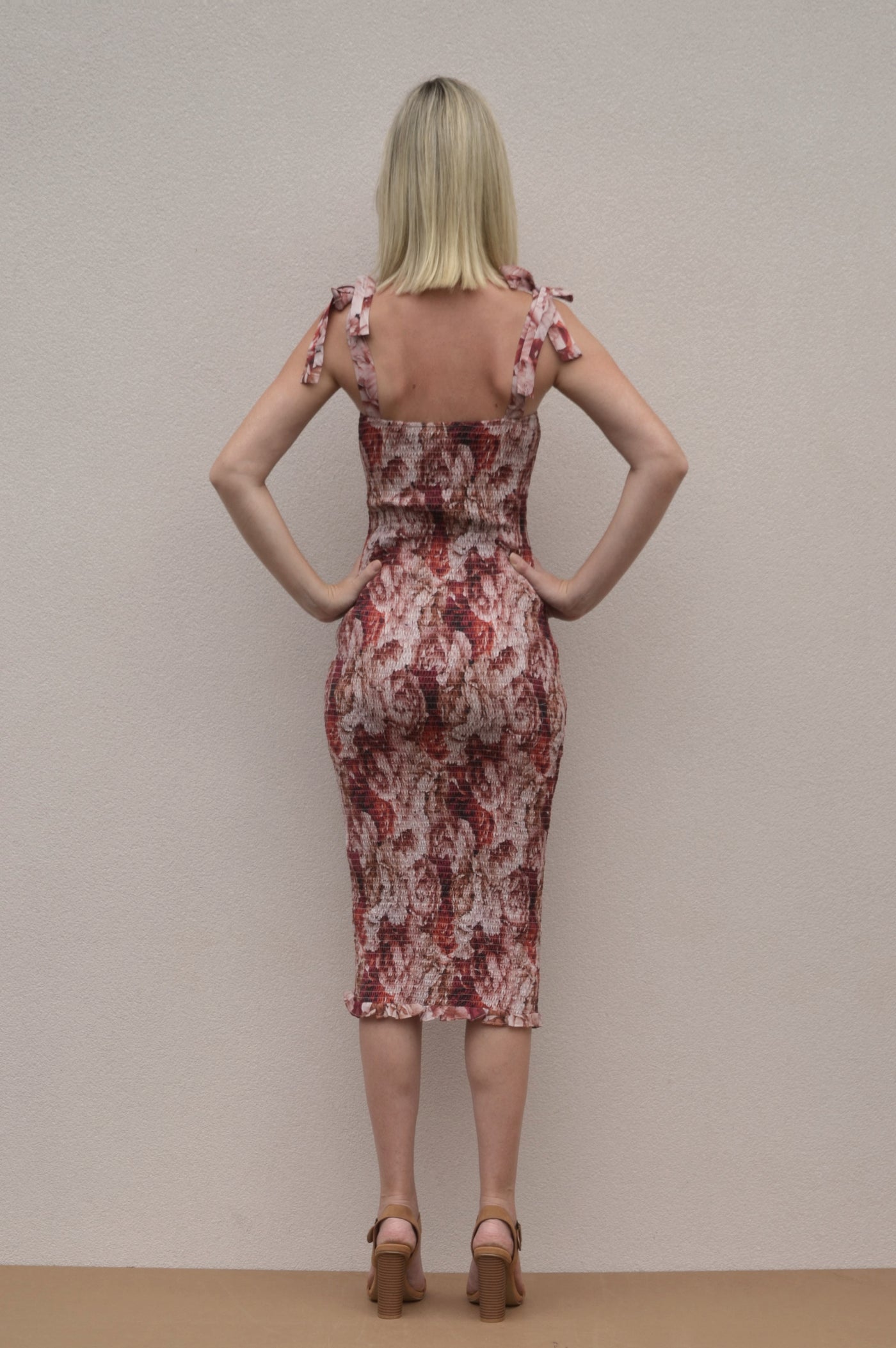 A shirred bodycon dress with tie up straps. A midi length dress with a red floral pattern