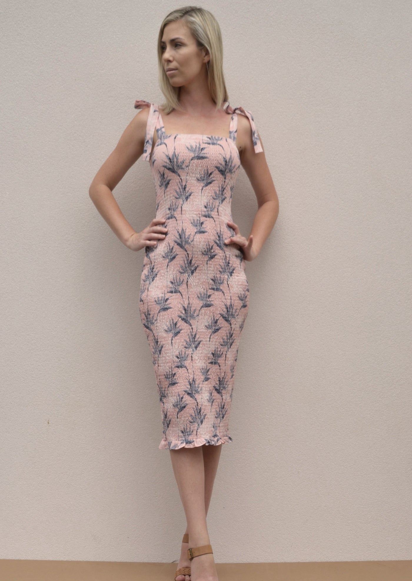 A shirred bodycon dress with tie up straps. A midi length dress with a light pink pattern.